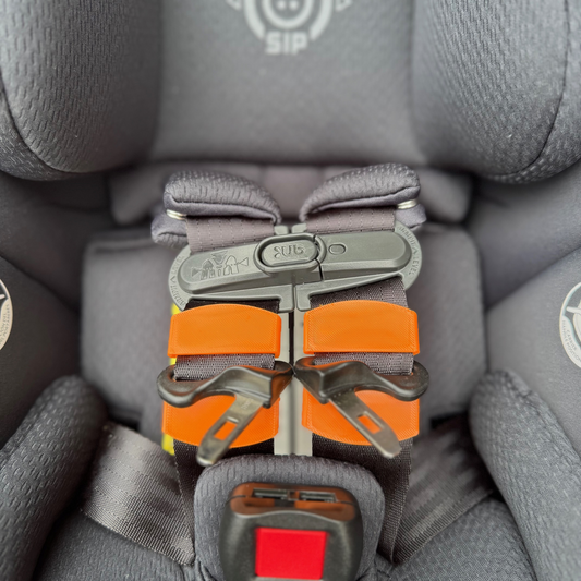 Close-up of a car seat belt buckle with orange strap accessory on a gray car seat.